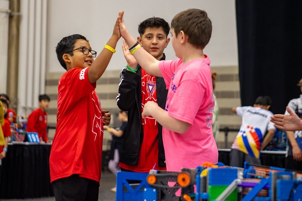 Three students from two different teams high five to celebrate a match beside a VIQRC field.