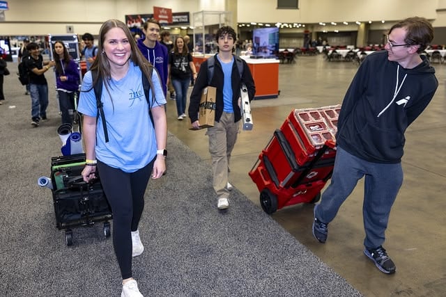 A V5 team drags and carries crates of parts, pieces, and robots to their pit at an event.