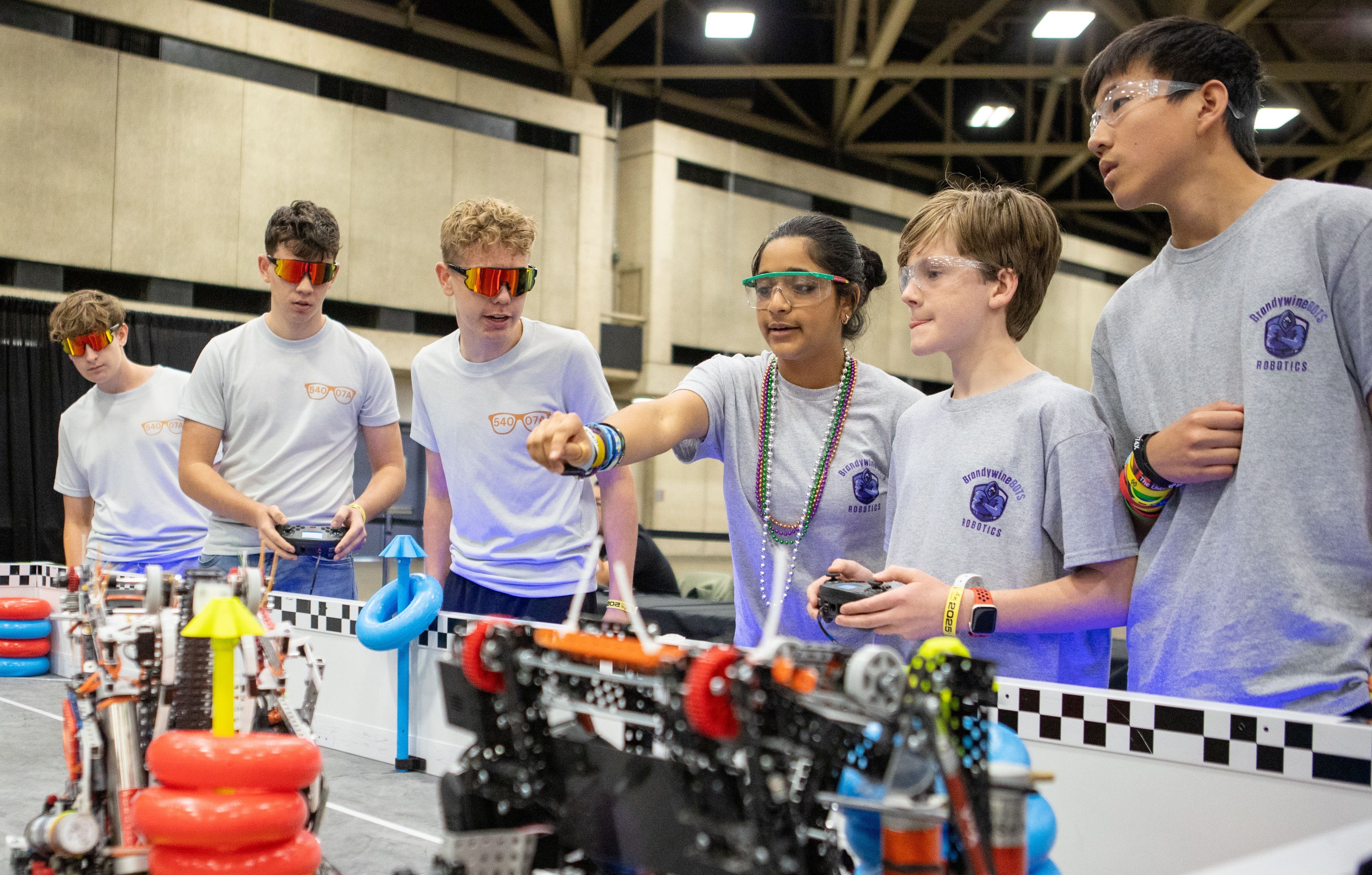 6 students at a V5RC field looking at their robots and pointing to indicate discussion about the game that is in progress.