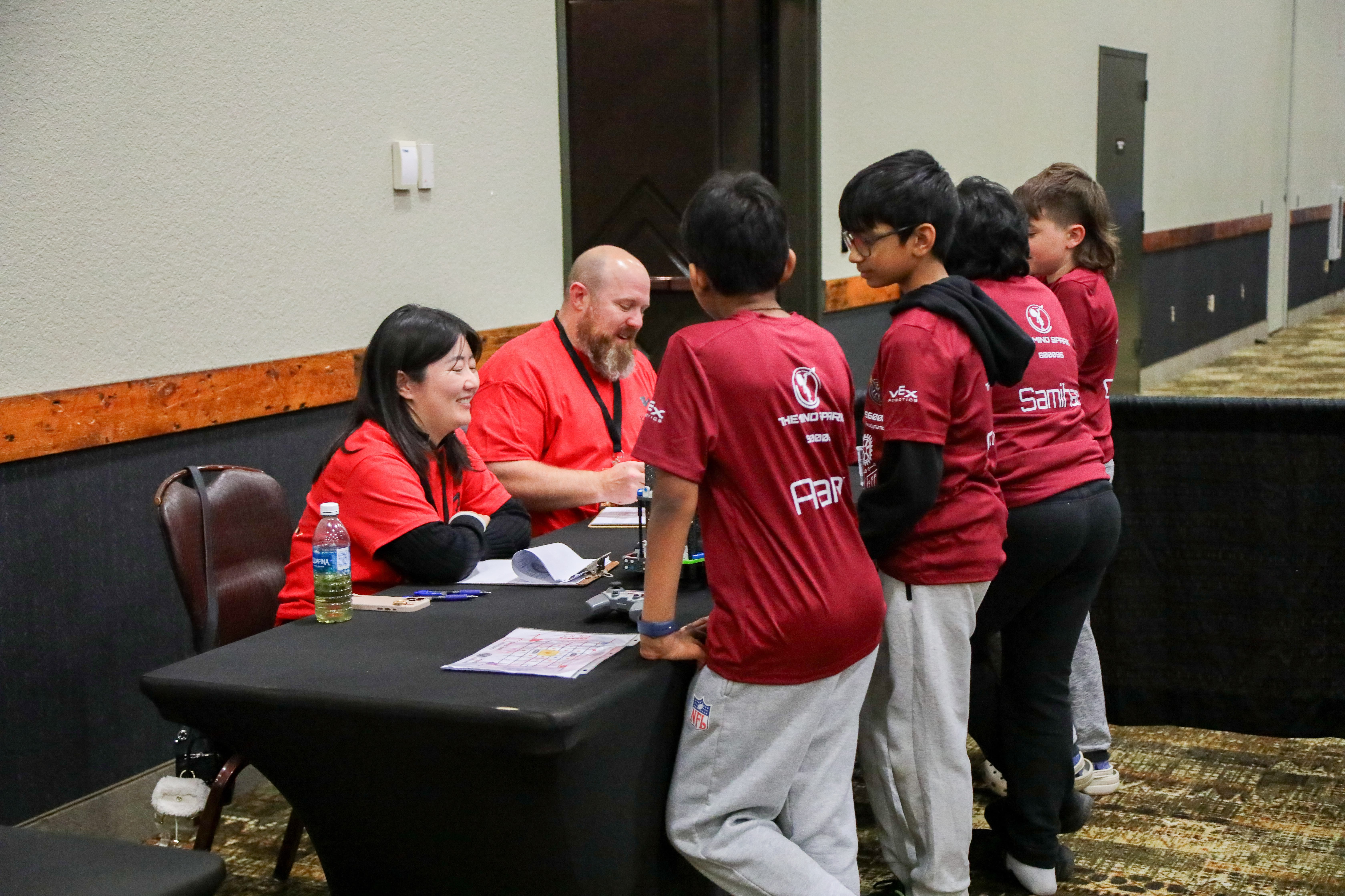 Two judges seated at a table smile as they talk with two IQ team members.