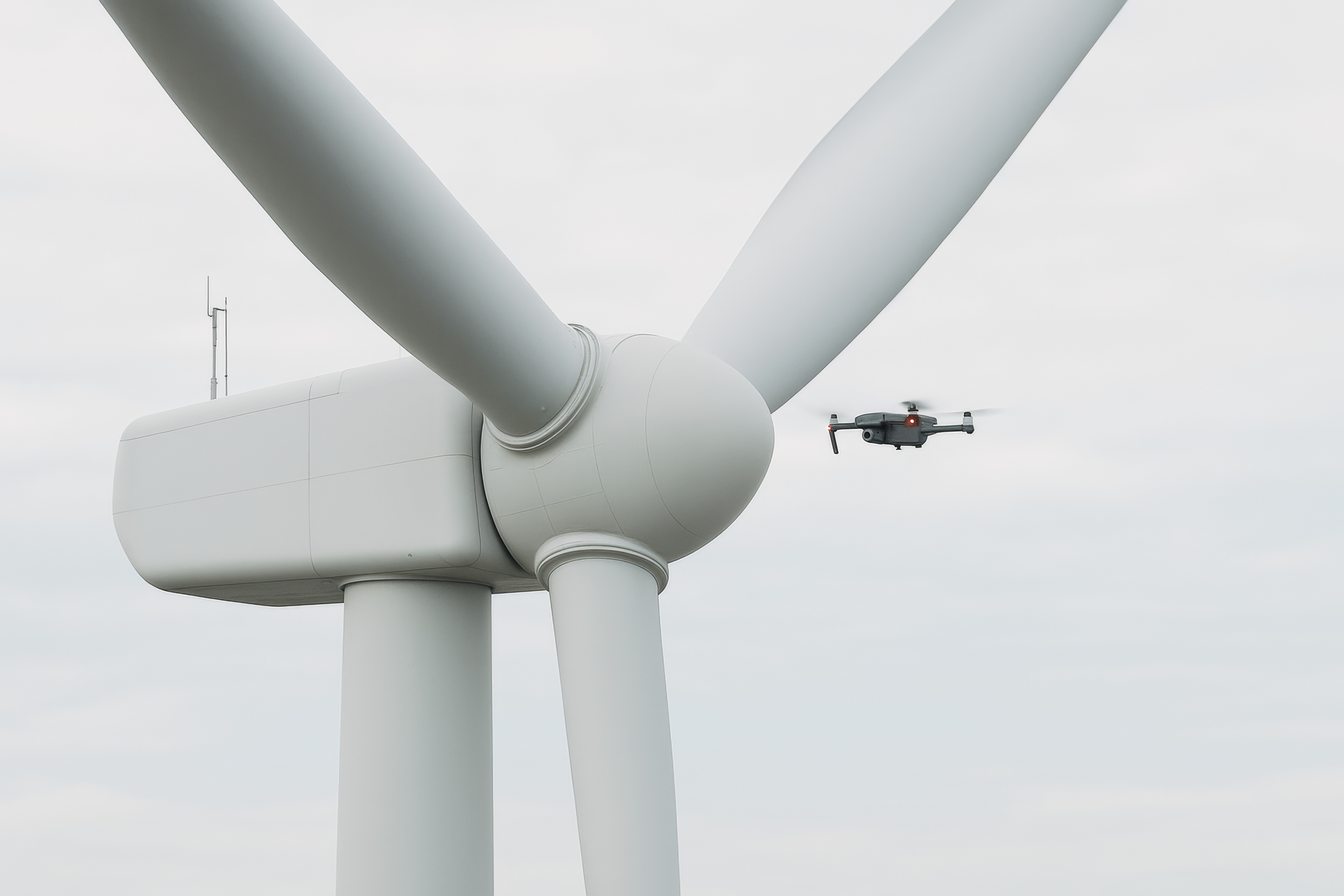 A drone flies in front of a giant wind turbine taking images high above the ground.
