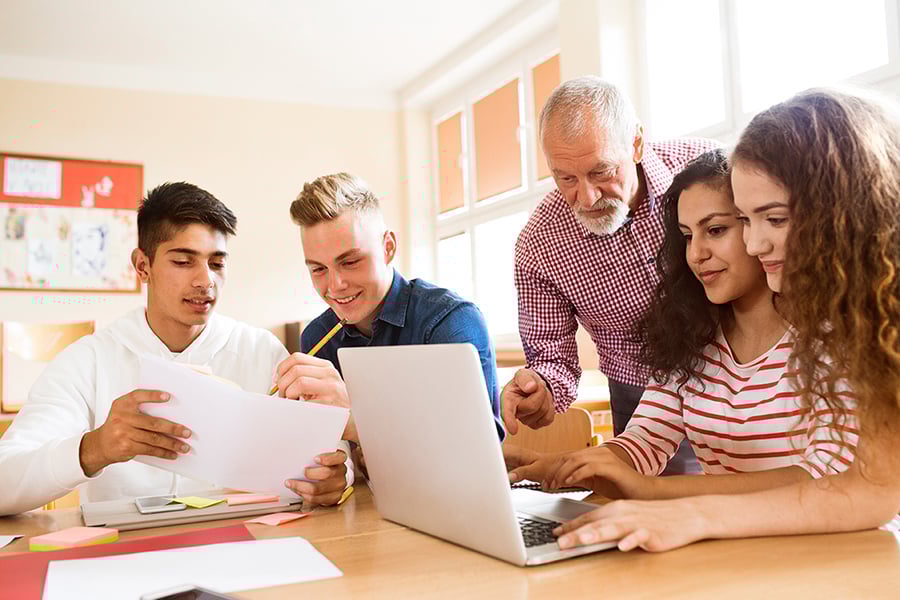 Four high school students working with each other and their teacher.