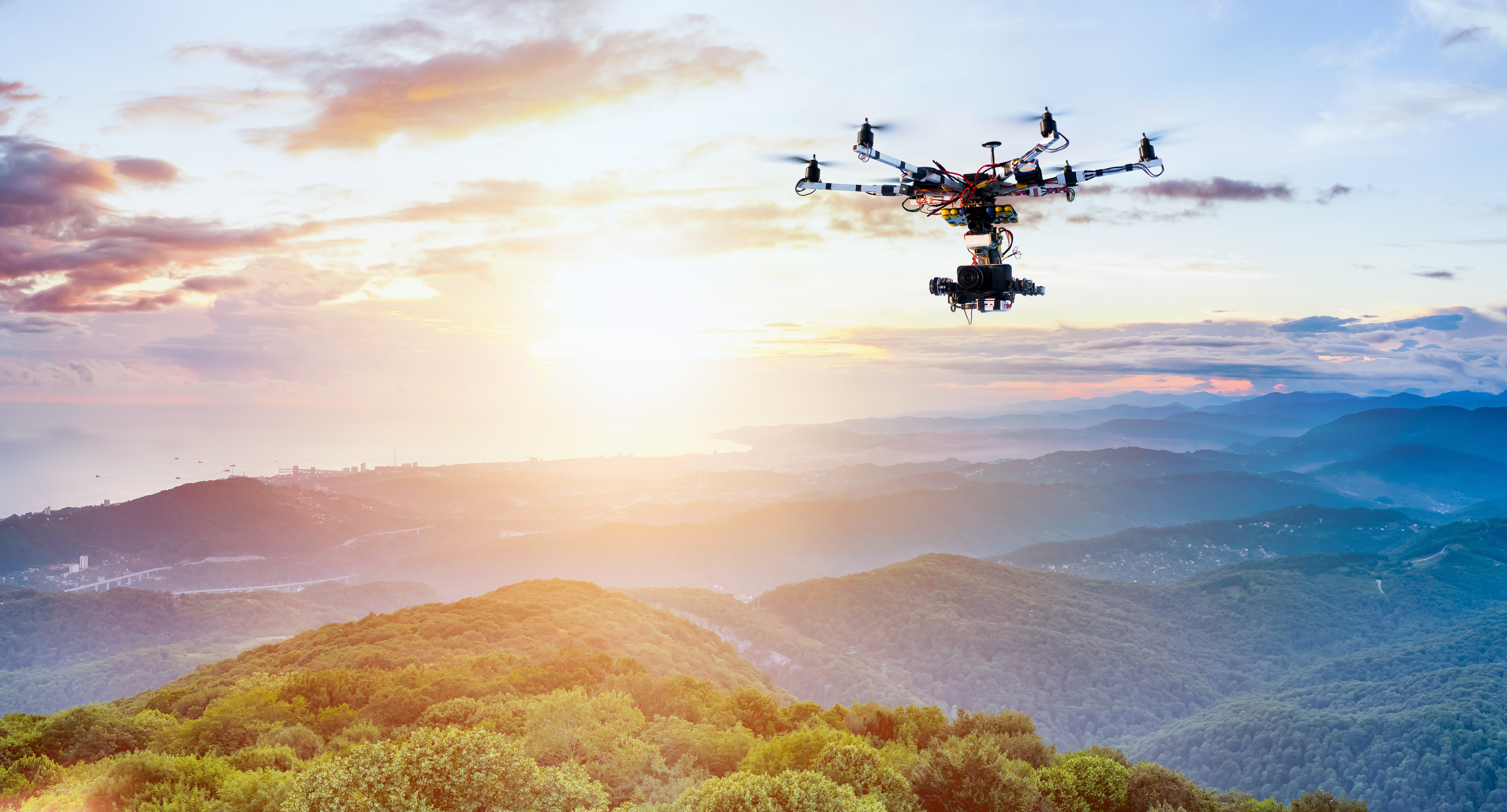 A drone with a camera rig attached flies over a mountainous landscape capturing video footage.
