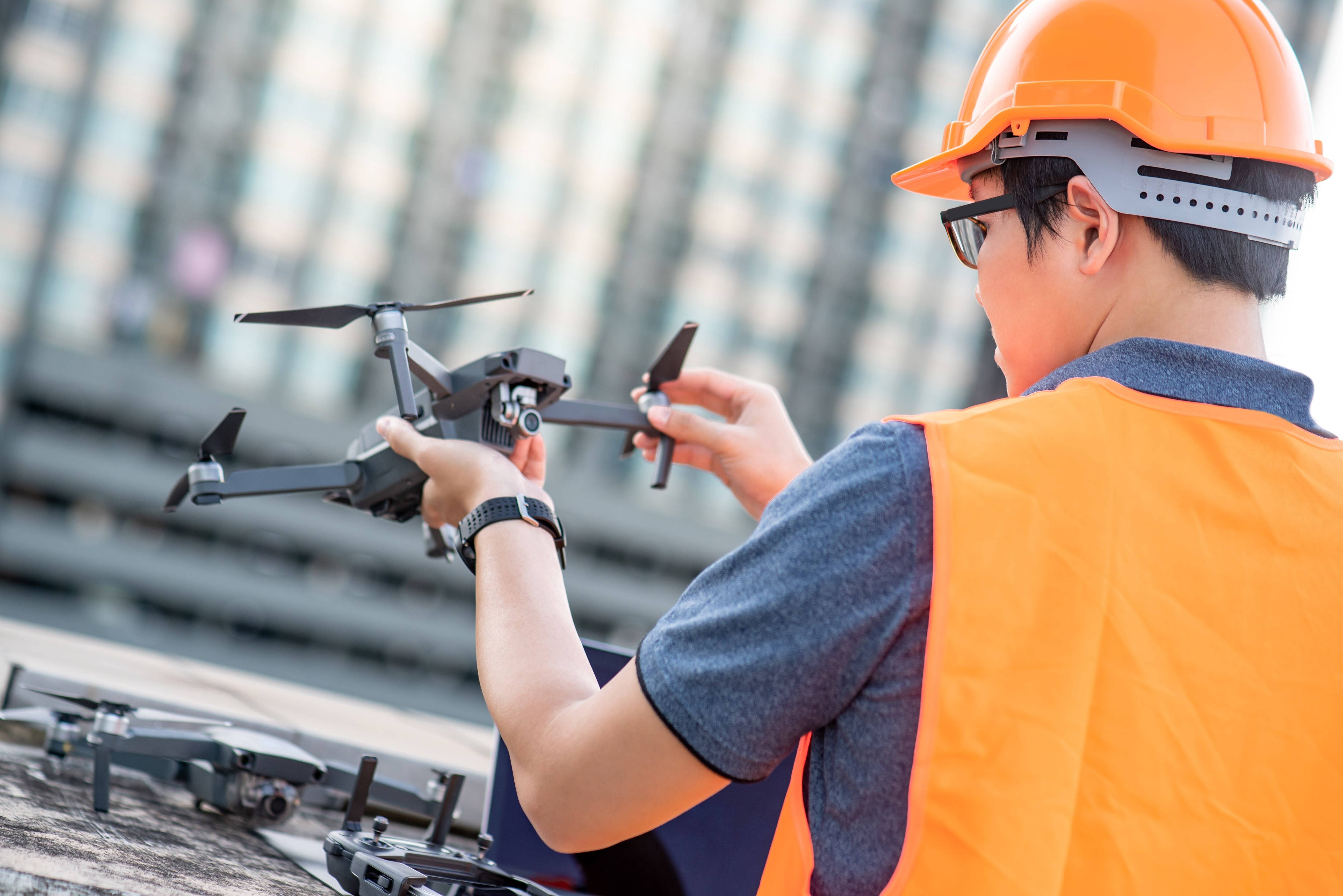 Young man in construction safety gear inspects a drone.
