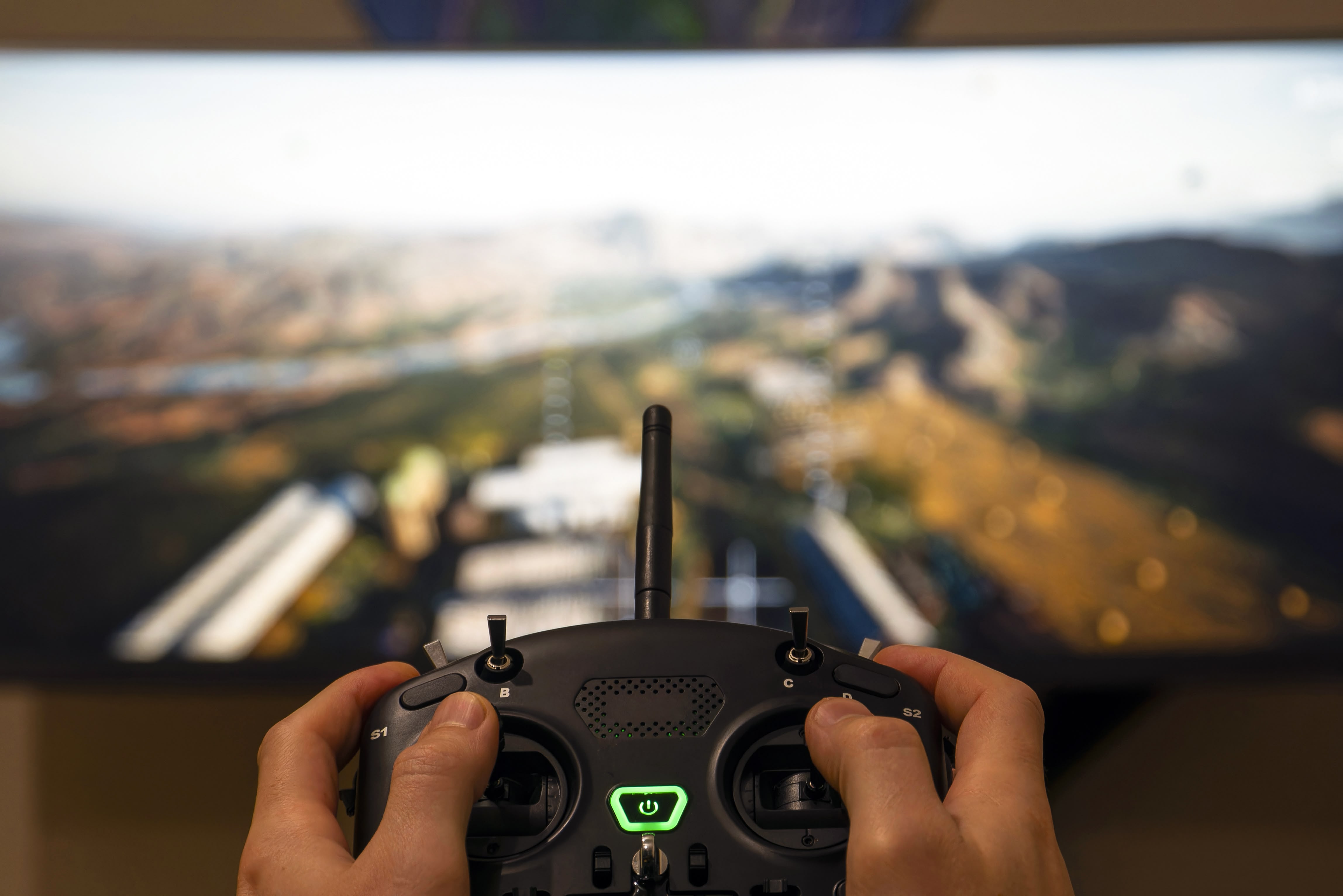 Drone controller in front of a screen with two hands manipulating the controls.