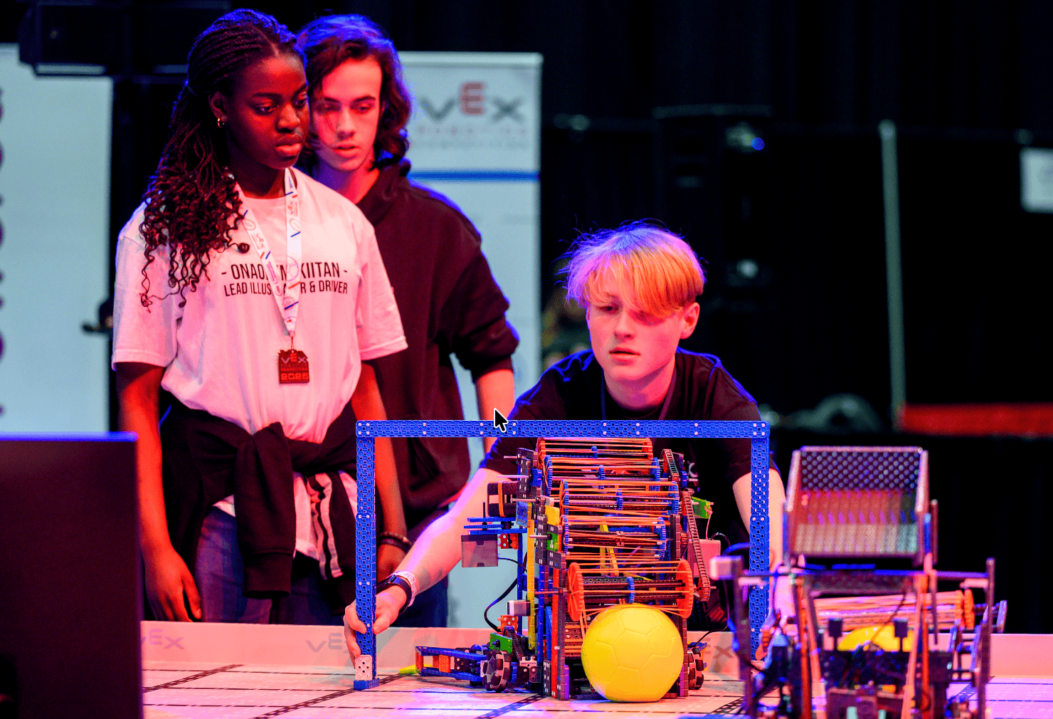 2 team members observe as a third uses the IQ sizing tool to check the size of their IQ robot at a competition.