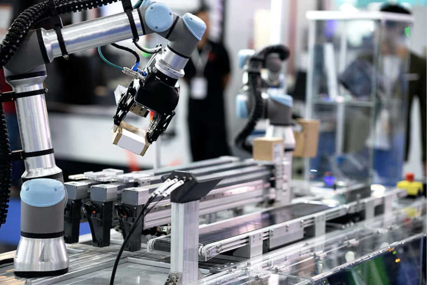 A robotic arm with a gripper moving a box in a factory.