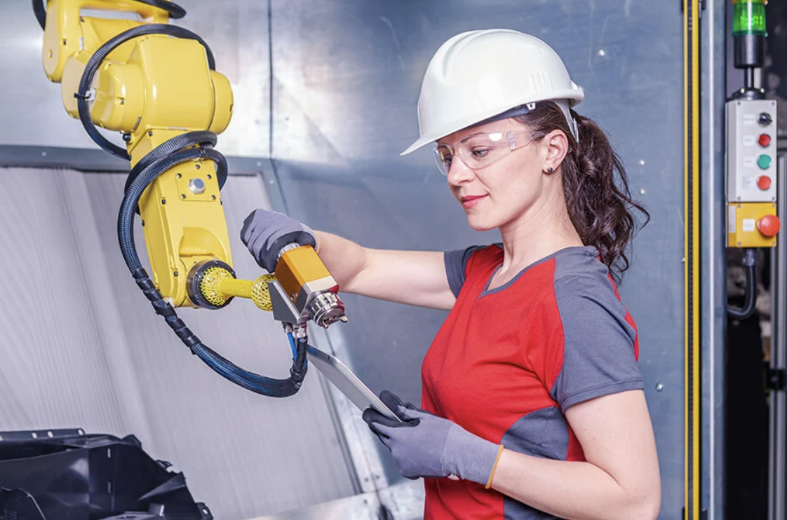 A photo of a worker handling a robotic arm, with a controlled stop button and indicator lights to the right.