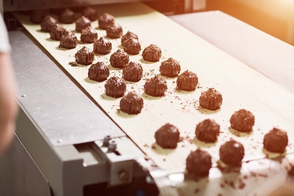 A conveyor belt moves chocolates along a mechanical assembly line.
