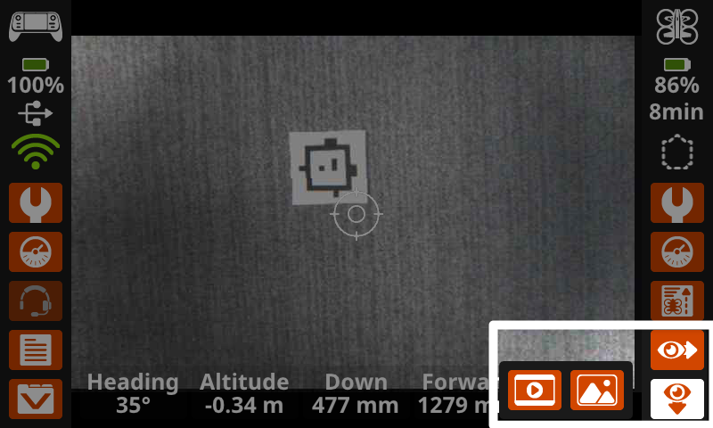 The VEX AIR Drone Controller screen shows the down camera view in the center of the screen, and the eye icon buttons in the lower right corner are highlighted, indicating what to select to capture images and video.