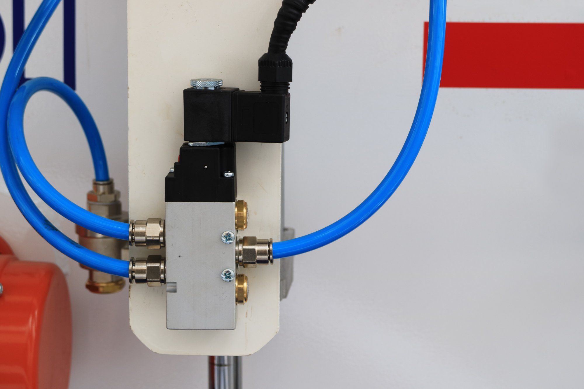 Pneumatic solenoid mounted on a factory wall with tubing extending from both sides.